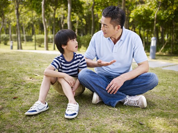Father speaking to son while sitting on grass